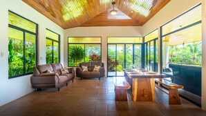 Amplia sala de estar con techo de madera, ventanas grandes y una mesa de madera central con bancos.