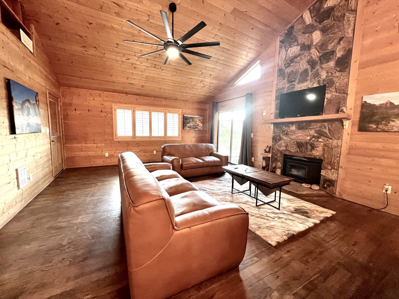 A log cabin interior with a sofa set, a fireplace, and a ceiling fan.