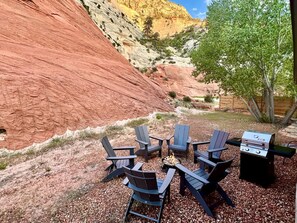 An outdoor seating area with Adirondack chairs and a grill, set against a backdrop of red rock formations. - Serene Cabin Perfect for Small Group in Orderville, Utah (Orderville)