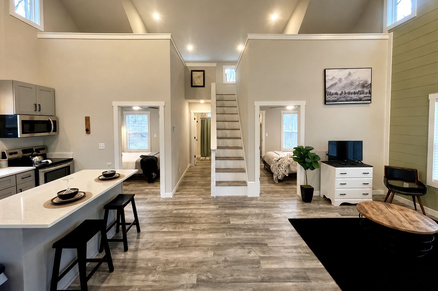 A modern kitchen with a central island, a dining area, and a staircase leading to a bedroom.