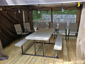 A covered outdoor dining area with a table and benches, surrounded by walls and a wooden deck. - Beautiful Cottage Nestled Amidst Trees in Wellston, Michigan (Wellston)
