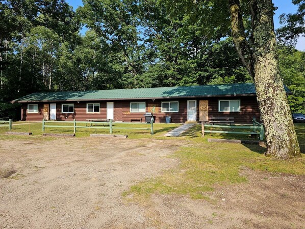 A rustic cabin with a green roof, a gravel driveway, and a wooden fence. - Beautiful Cottage Nestled Amidst Trees in Wellston, Michigan (Wellston)