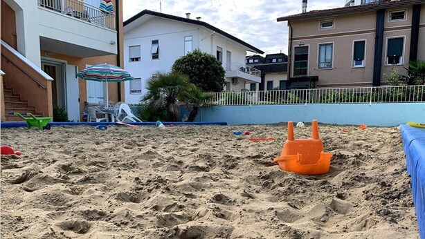 A sandy beach area with a small orange sandcastle and a blue poolside area. - Apartment 'Valentina 1 - Ground Floor' with Shared Pool, Wi-Fi and Air Conditioning (Lido di Jesolo)