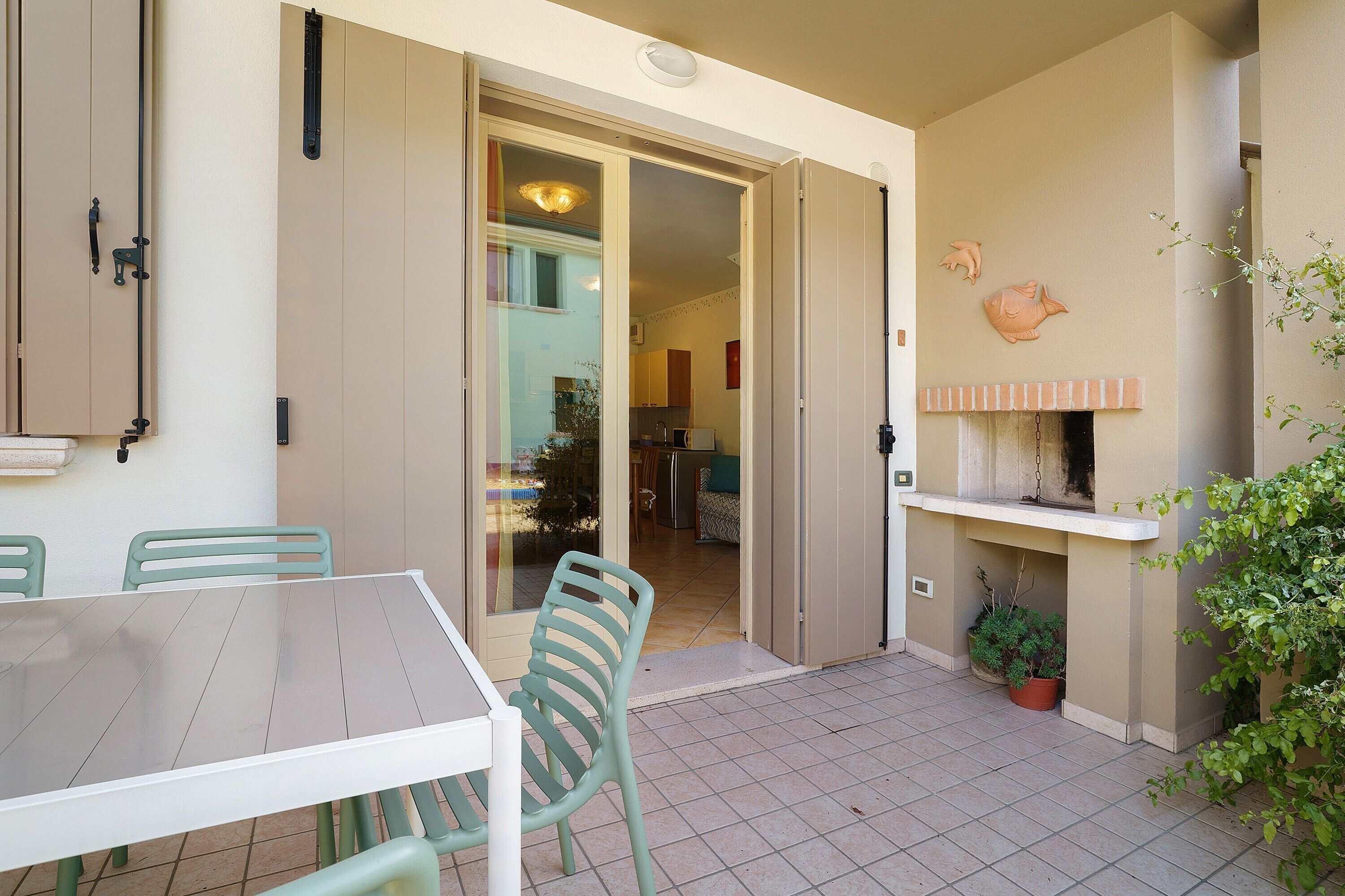 An open sliding door leading to a kitchen, a dining table with chairs, and a small potted plant.
