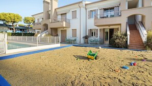En boligbygning med swimmingpool, udendørs siddepladser og et sandlegeområde.