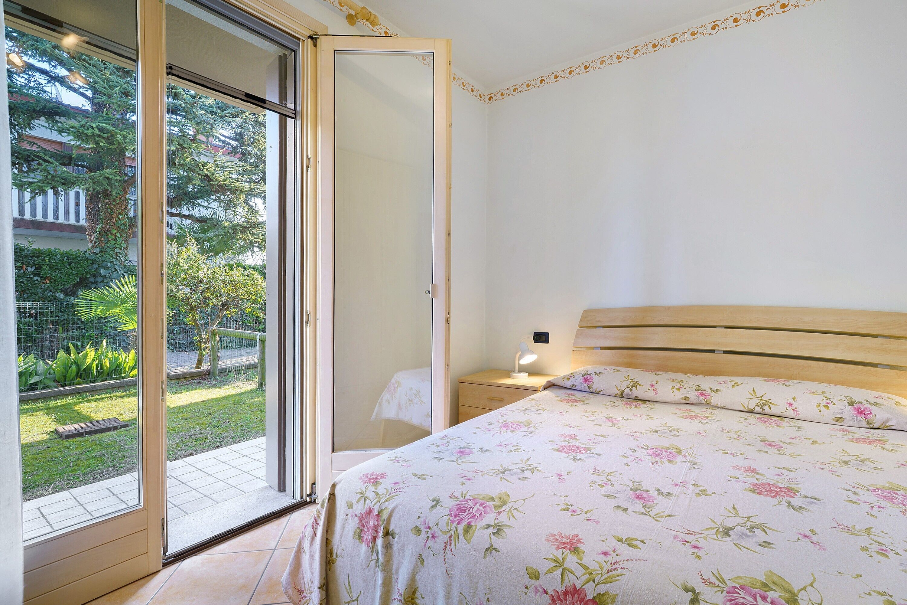 Una camera da letto con un letto, un comodino, una lampada e una porta a vetri scorrevoli che dà sul giardino.