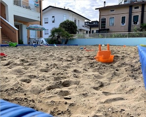 A sandy beach area with a small orange sandcastle and a blue poolside area. - Apartment 'Valentina 1 - Ground Floor' with Shared Pool, Wi-Fi and Air Conditioning (Lido di Jesolo)