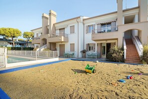 A residential building with a swimming pool, outdoor seating, and a sandy play area. - Apartment 'Valentina 1 - Ground Floor' with Shared Pool, Wi-Fi and Air Conditioning (Lido di Jesolo)