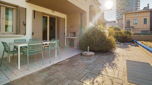 Eine Terrasse mit Tisch und Stühlen, ein kleiner Garten und ein Gebäude mit Balkon.
