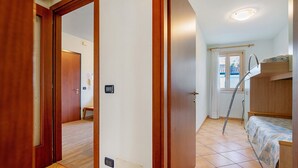 Quarto com beliche, porta que dá para outro espaço e janela com cortina.