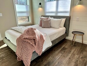 A bed with a grey headboard, a pink knitted blanket, and a round side table with a lamp. - New Mountain Tiny Retreat with Beautiful Deck in Tennessee (Monteagle)