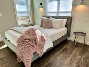 A bed with a grey headboard, a pink knitted blanket, and a round side table with a lamp. - New Mountain Tiny Retreat with Beautiful Deck in Tennessee (Monteagle)