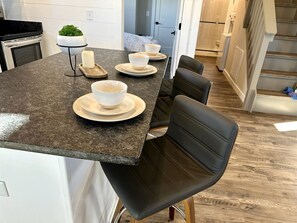 A kitchen with a granite countertop, white cabinets, a black chair, and a small potted plant. - New Mountain Tiny Retreat with Beautiful Deck in Tennessee (Monteagle)