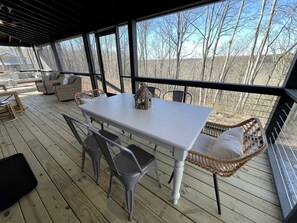 A covered outdoor area with a table and chairs, wicker furniture, and large windows. - New Mountain Tiny Retreat with Beautiful Deck in Tennessee (Monteagle)
