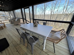 A covered outdoor area with a table and chairs, wicker furniture, and large windows. - New Mountain Tiny Retreat with Beautiful Deck in Tennessee (Monteagle)