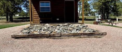 Una cabaña de madera con camino de grava y un pozo de fuego de piedra al frente.