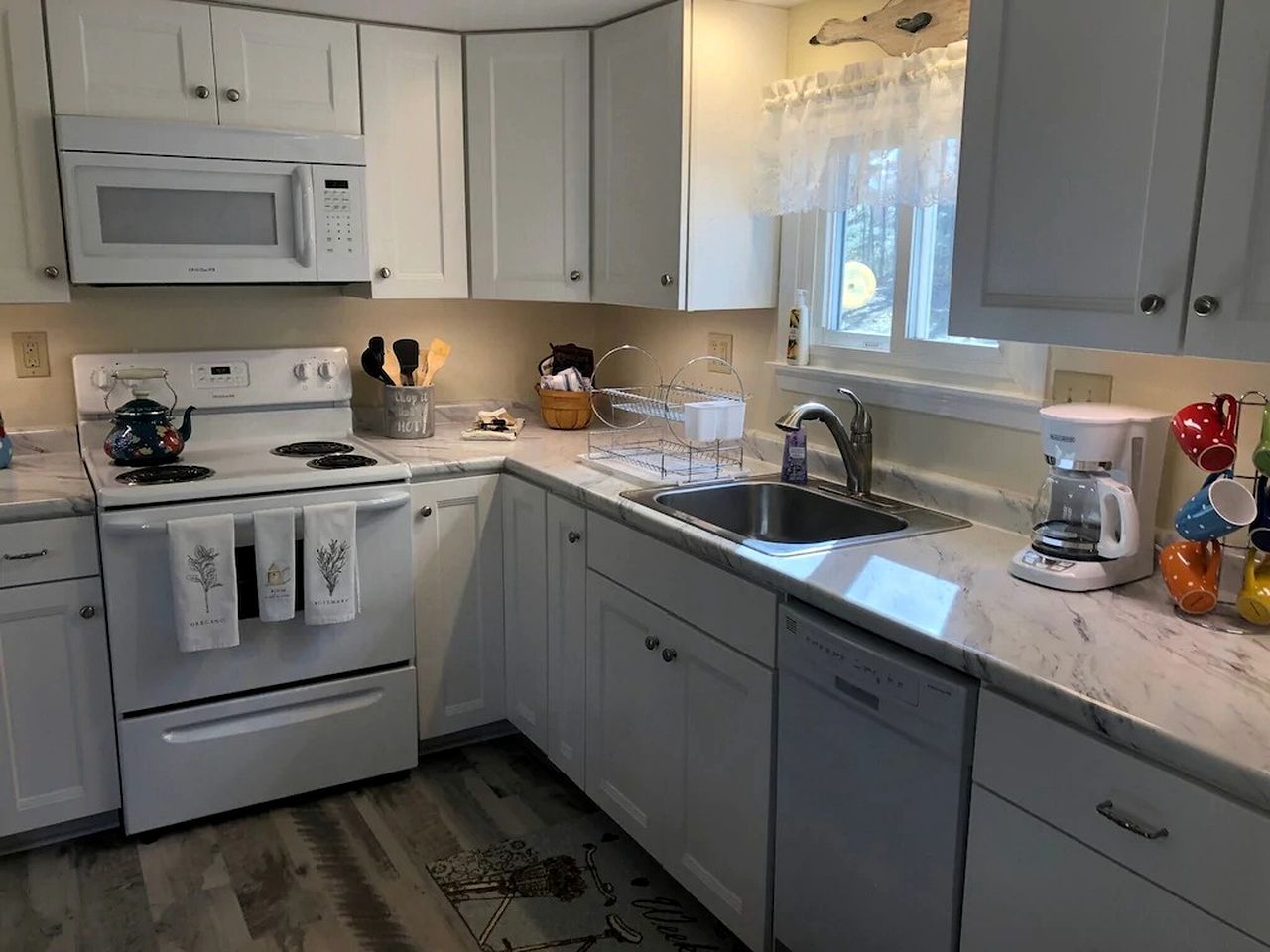 A kitchen with white cabinets, a microwave, stove, sink, and a coffee maker.