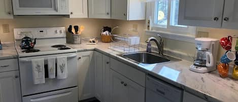A kitchen with white cabinets, a microwave, stove, sink, and a coffee maker.