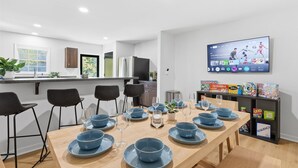 Een moderne keuken met een eethoek, gedekt voor een maaltijd, een tv waarop sport wordt vertoond, en een plank met gezelschapsspellen.