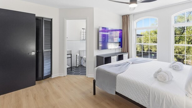 Een moderne hotelkamer met een bed, een televisie, een plafondventilator en een raam met uitzicht op bomen.