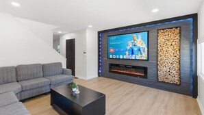 Een moderne woonkamer met een grijze bank, een zwarte salontafel, een flatscreen-tv aan een wand met een houtblok decoratie en een open haard.