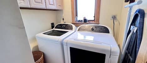 A compact laundry room with two front-loading washing machines, a window above the machines, and a door with a towel rack.