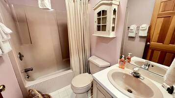 A bathroom with a bathtub, toilet, shower curtain, and a sink with a mirror.