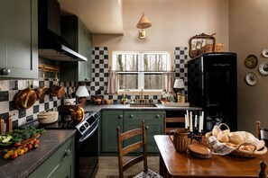 A kitchen with green cabinets, a black refrigerator, copper cookware, and a window with curtains. - Secluded Cabin in the Woods in Monteagle, Tennessee (Monteagle)