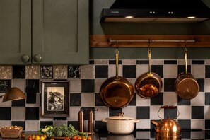 A kitchen with a checkered tile backsplash, hanging copper cookware, a brass kettle, and a framed picture. - Secluded Cabin in the Woods in Monteagle, Tennessee (Monteagle)