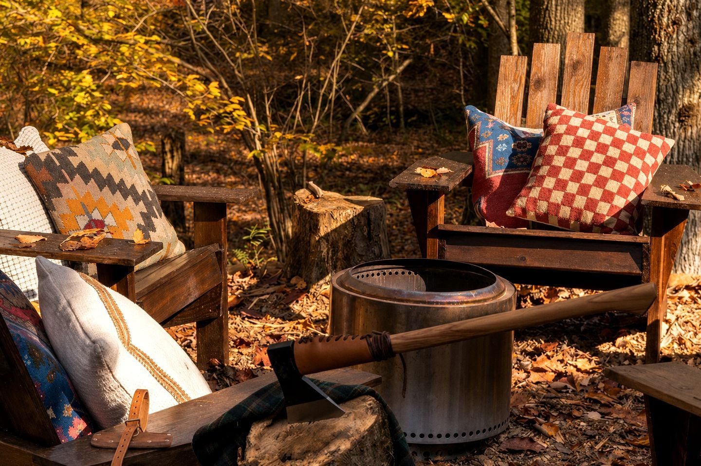 A rustic outdoor seating area with a metal cooking pot, a wooden chair with a checkered cushion, and a bench with patterned cushions.