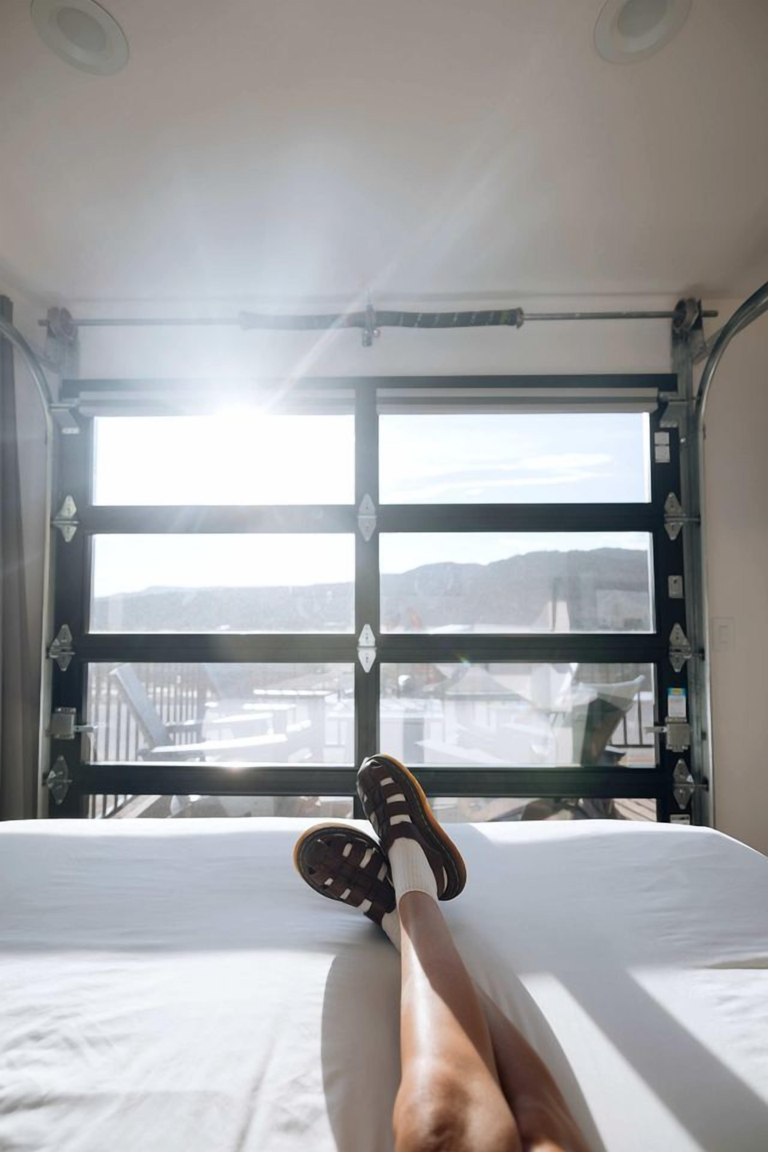 Una cama con vista a un paisaje urbano a través de un ventanal.
