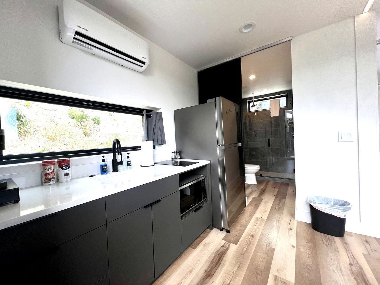 A modern kitchen with a built-in oven, a stainless steel refrigerator, and a window providing natural light.