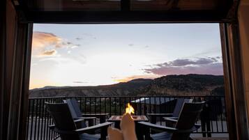 Un balcon donnant sur un paysage de montagnes au coucher du soleil, une table avec une bougie allumée et deux chaises.