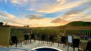 A hot tub with a pool, surrounded by chairs, and a view of the sky and landscape.