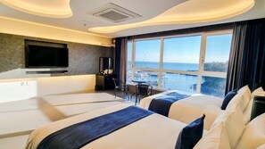 Habitación de hotel con dos camas, televisión, escritorio y vistas al mar.