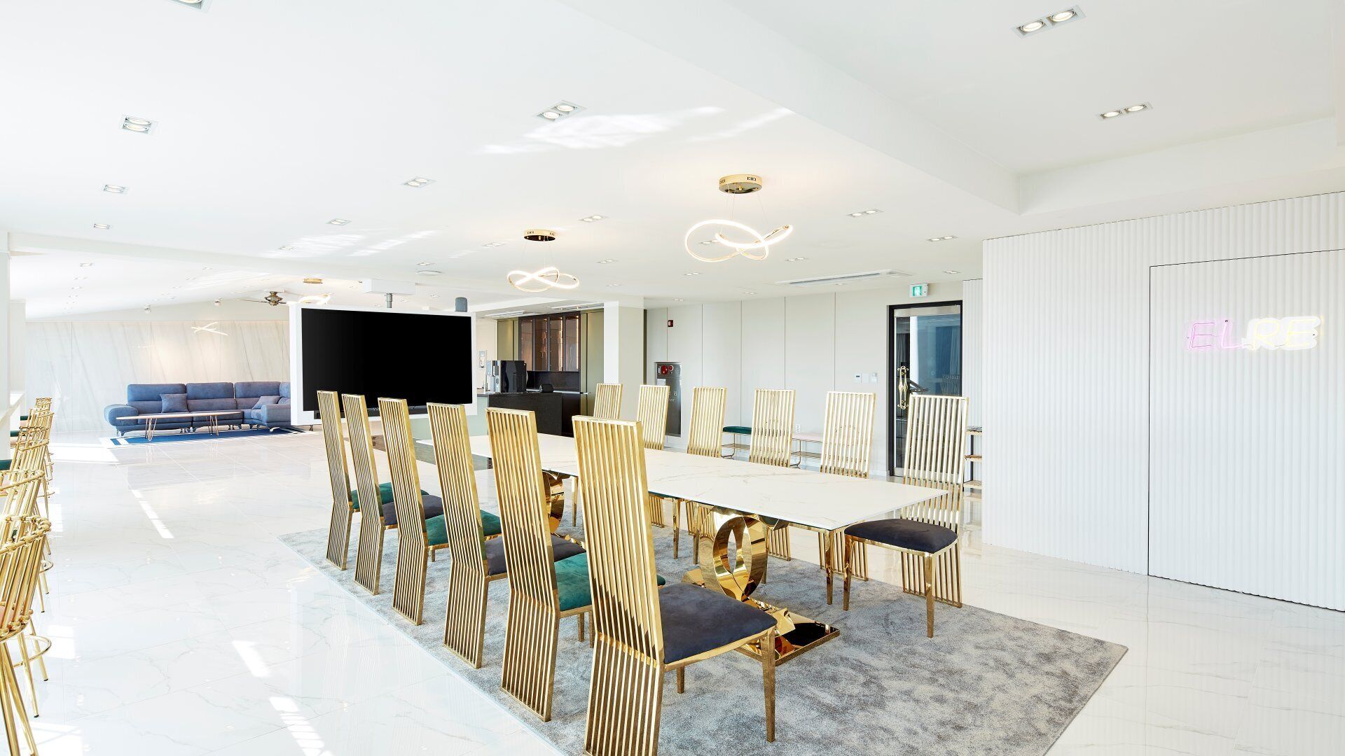 A modern conference room with a long table, golden chairs, and a large screen.