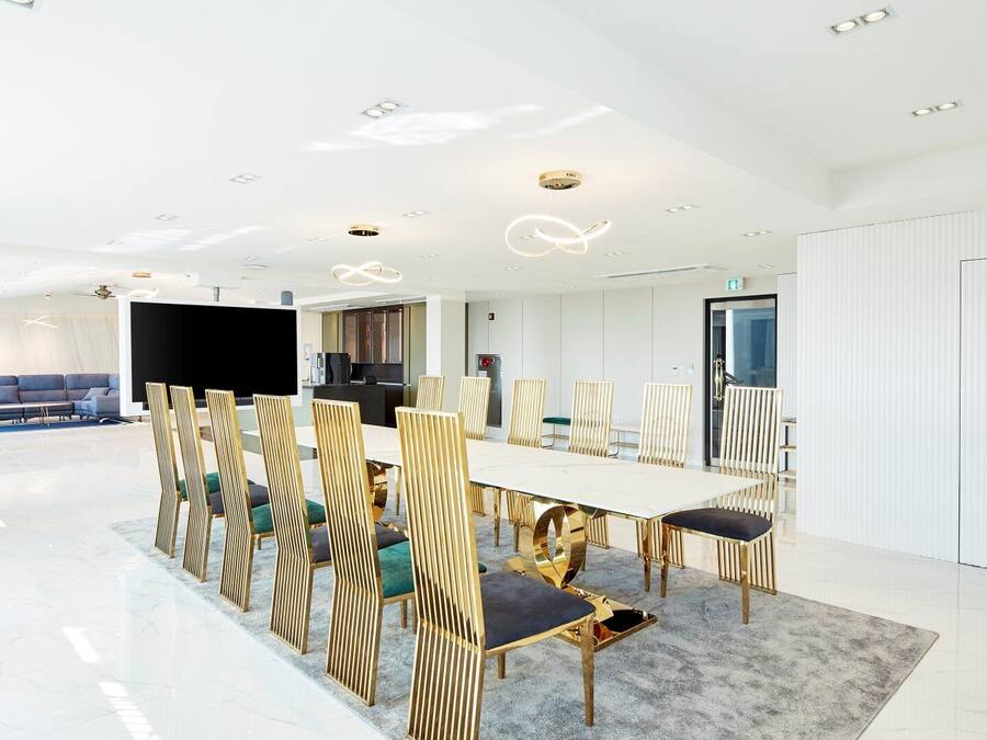A modern conference room with a long table, golden chairs, and a large screen.
