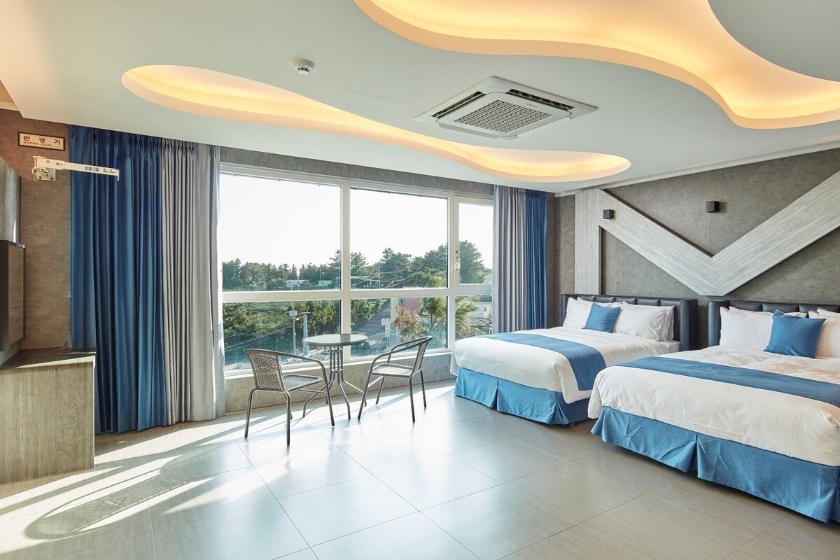 A modern hotel room with two beds, a balcony, and a view of the outdoors.