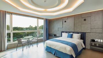 A modern hotel room with a large bed, a seating area with chairs, and a view of the outdoors.