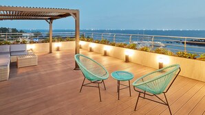 A wooden deck with wicker chairs and a table, overlooking a marina with boats and a clear view of the ocean. - Elren Hotel (Seogwipo)