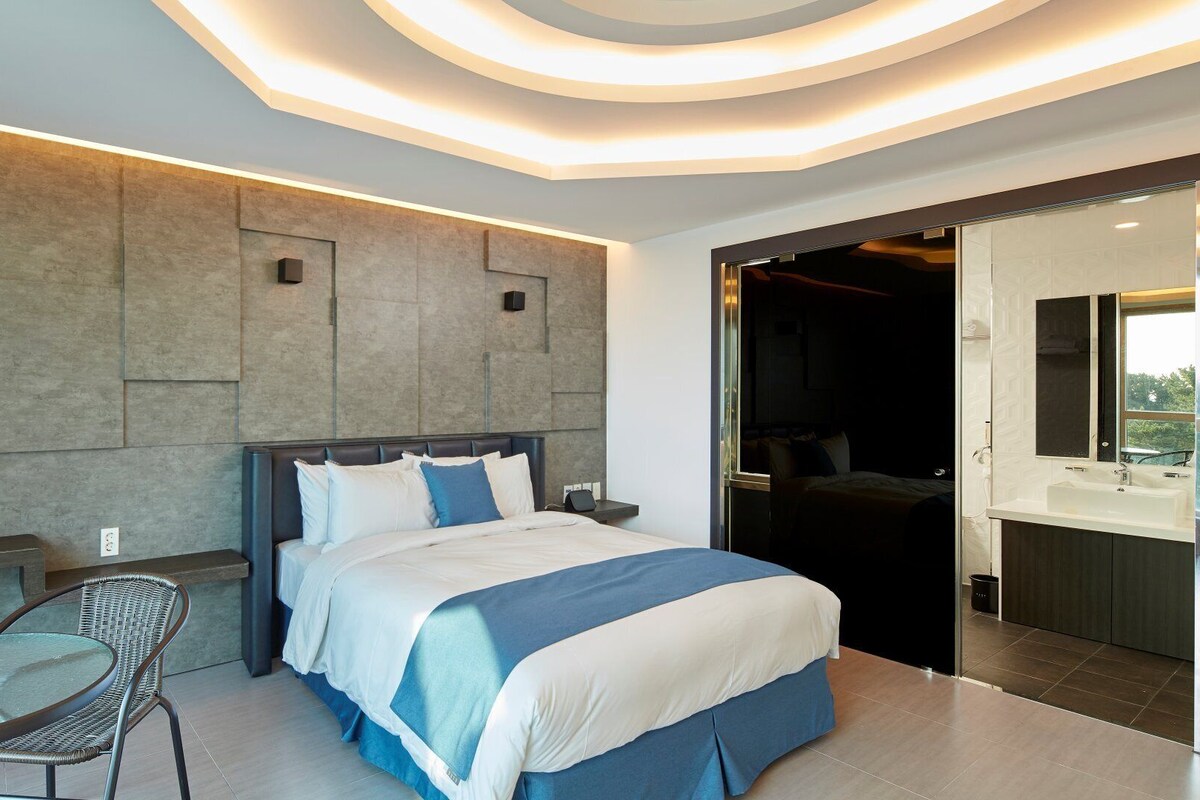 A modern hotel room with a large bed, a small table, and a seating area.
