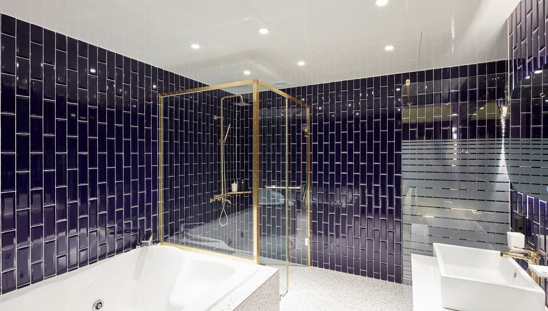 A modern bathroom with a glass-enclosed shower, two white sinks, and dark tiled walls.
