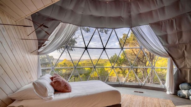 A bedroom with a large window, a bed, and a view of trees.