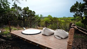 Una terraza de madera con jacuzzi, cojines a rayas y vistas del bosque circundante.
