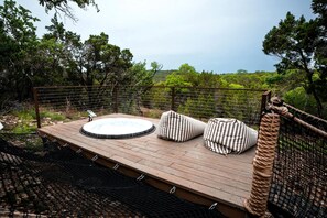 Een houten terras met een jacuzzi, gestreepte kussens en uitzicht op het omliggende bos.