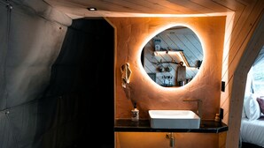 A compact bathroom with a round mirror, a white sink, and a wooden vanity.