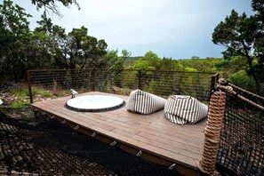 Une terrasse en bois avec un jacuzzi, des coussins à rayures et une vue sur la forêt environnante.
