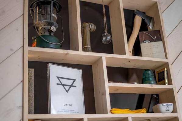 A wooden shelf with various items including a book titled 'UKIYO,' a fire starter, and a metal container. - Quality Time in Nature: Marble Falls Luxury Glamping for Families (Marble Falls)