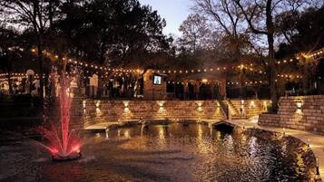 A nighttime outdoor area with a fountain, brick walls, and string lights.