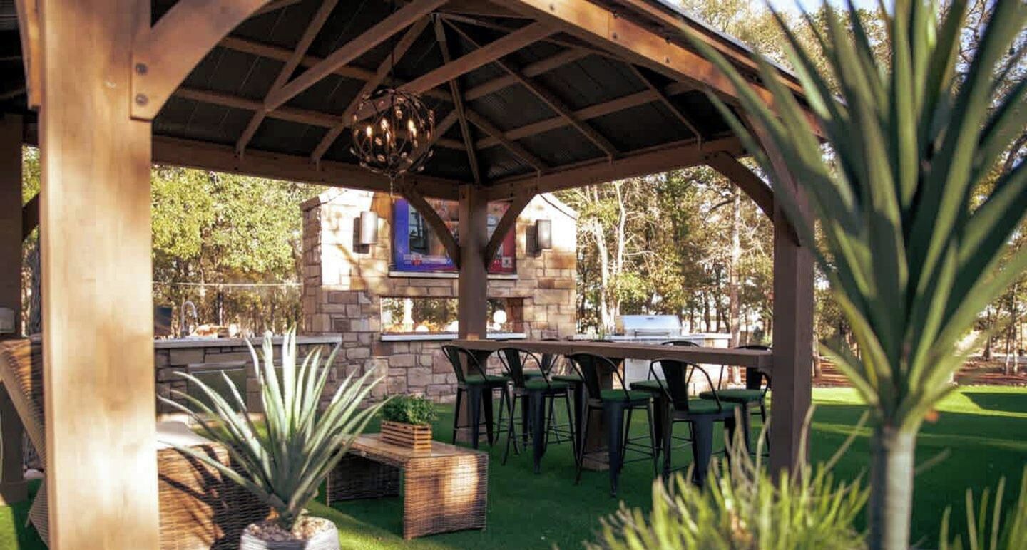 Une terrasse extérieure dotée d’une pergola en bois, de murs en pierre et d’un barbecue.